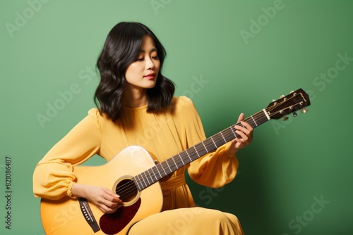 Portrait of a tender asian woman in her 40s playing the guitar over solid color backdrop photo