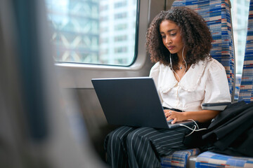 Businesswoman Commuting To Work On Train Sitting Working On Laptop Wearing Earphones