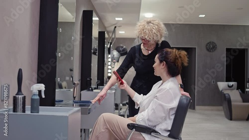 The client communicates with the hairdresser and shows a photo on the phone. Haircut and hairstyle done by a professional in a hair salon. High quality 4k footage photo