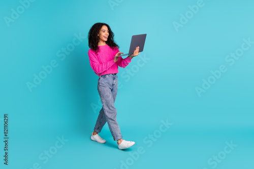 Full size photo of pretty teen girl hold netbook walk wear trendy pink outfit isolated on aquamarine color background