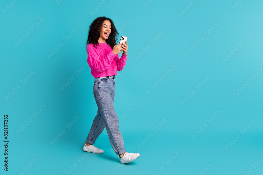 Full size photo of pretty teen girl hold device walking wear trendy pink outfit isolated on aquamarine color background Full size photo of pretty teen girl hold device walking wear trendy pink outfit isolated on aquamarine color background