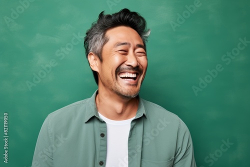 Portrait of a satisfied asian man in his 40s laughing isolated on solid pastel color wall photo