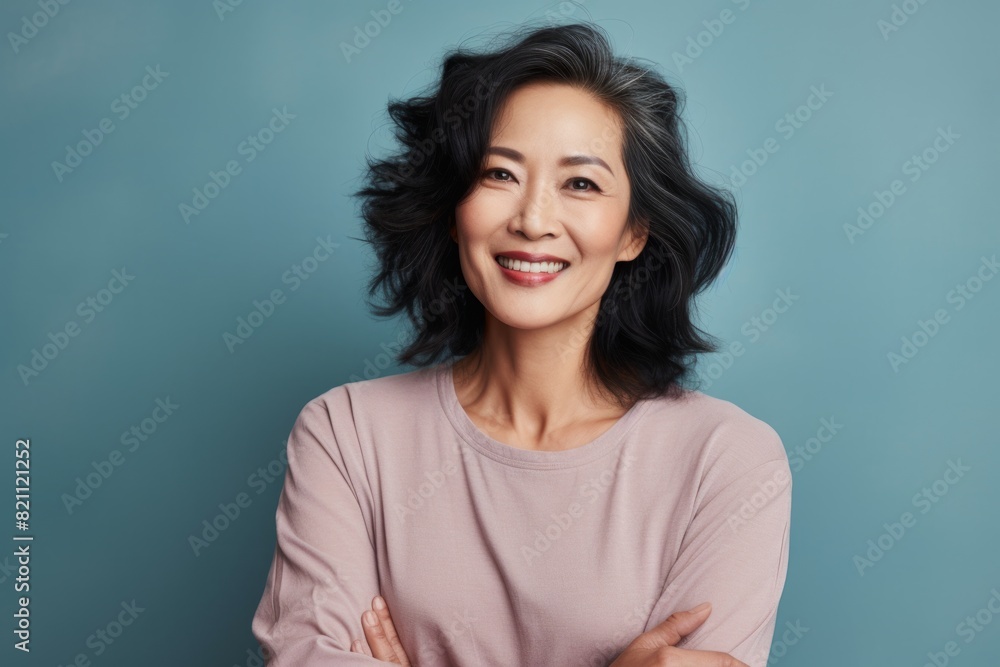 Portrait of a glad asian woman in her 50s smiling at the camera in solid pastel color wall Portrait of a glad asian woman in her 50s smiling at the camera in solid pastel color wall