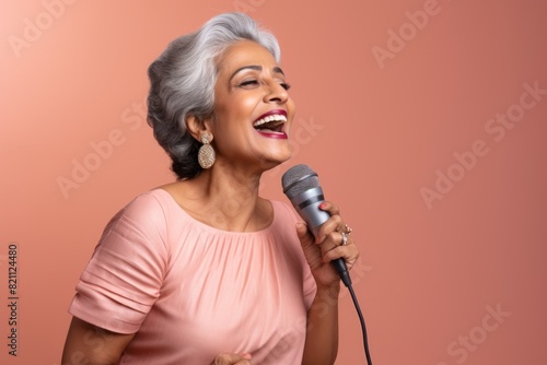 Wallpaper Mural Portrait of a tender indian woman in her 50s dancing and singing song in microphone while standing against solid pastel color wall Torontodigital.ca