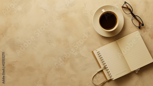 Minimalist workspace with a notebook, glasses, and a cup of coffee on a beige textured background