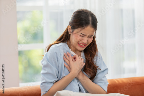 Woman clutching her chest with a pained expression, conveying heart-related or emotional distress. Indoor shot with natural lighting.