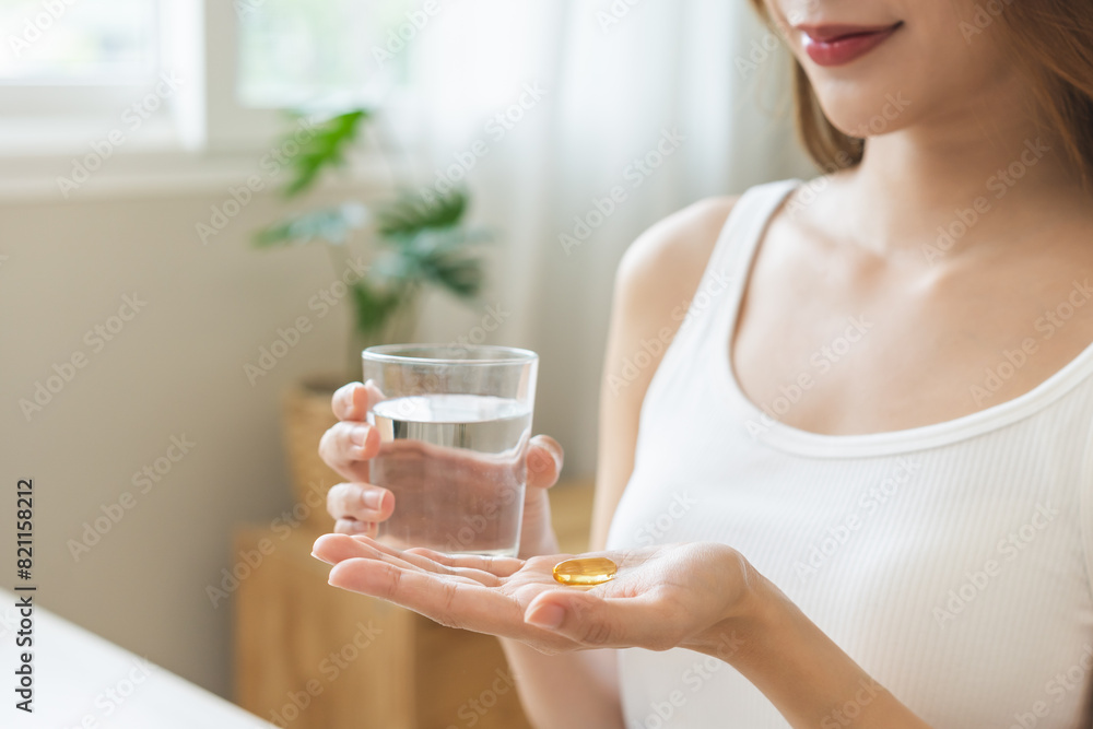 Dietary supplement, asian young woman, girl hand holding medical pill capsule, take or eat vitamin C, D for treatment for skin, hair and nail strengthen with glass of pure water at home, healthcare. Dietary supplement, asian young woman, girl hand holding medical pill capsule, take or eat vitamin C, D for treatment for skin, hair and nail strengthen with glass of pure water at home, healthcare.