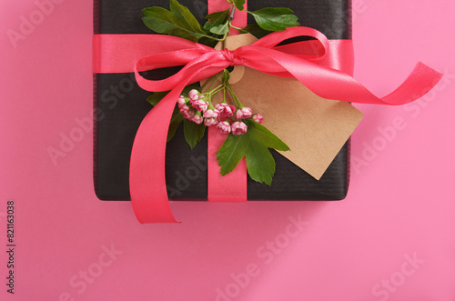 Black craft gift box with blank tag, hawthorn flowers on pink background. Place for your text