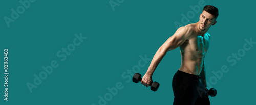 A man is lifting dumbbells while standing on a green background. He is focused and determined, with his muscles engaged. The mans form is precise as he performs the exercise, empty space © Prostock-studio