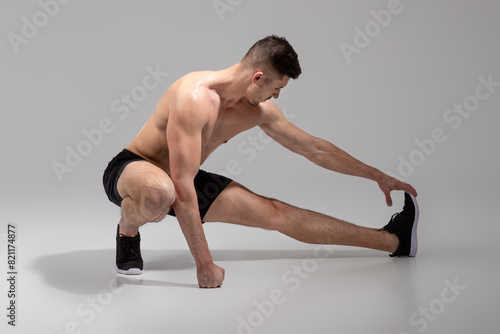 A fit, young man is seen stretching his leg muscles in a spacious, minimalist indoor gym, wearing black shorts and athletic shoes, practicing a deep lateral stretch to prepare for his workout routine photo