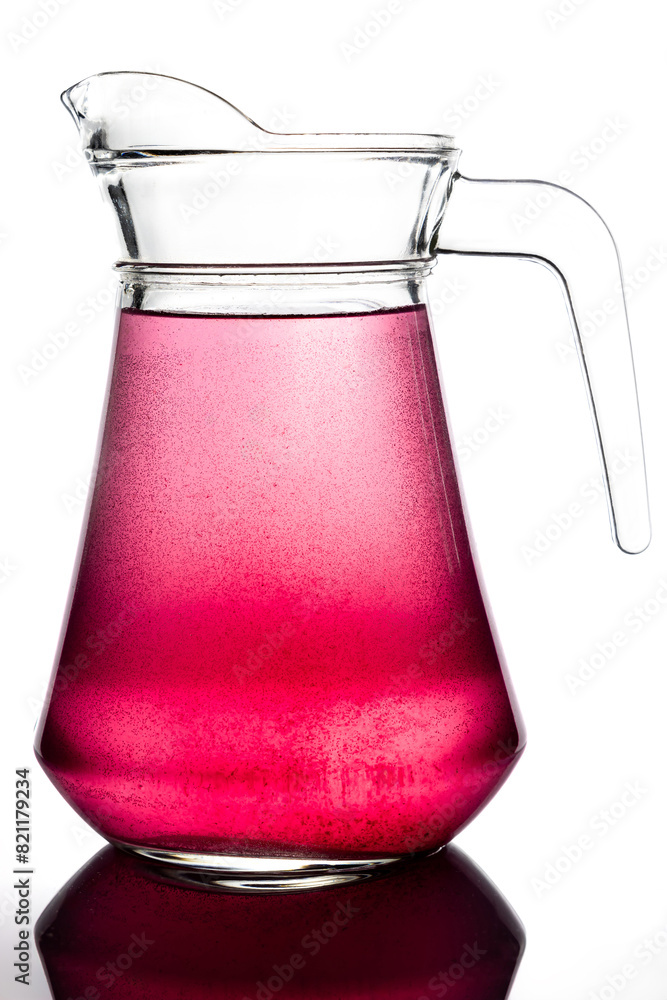 Transparent glass jug with red, translucent drink. A pitcher on a white background, photograph taken against the light