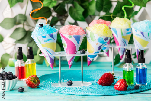 Colourful flavoured snow cones with fruit flavoured syrups in front.