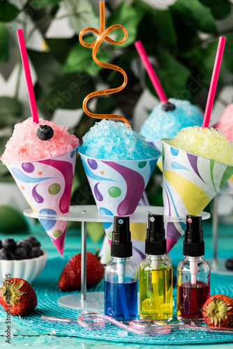 Colourful homemade snow cones with fruit flavoured syrups in front.