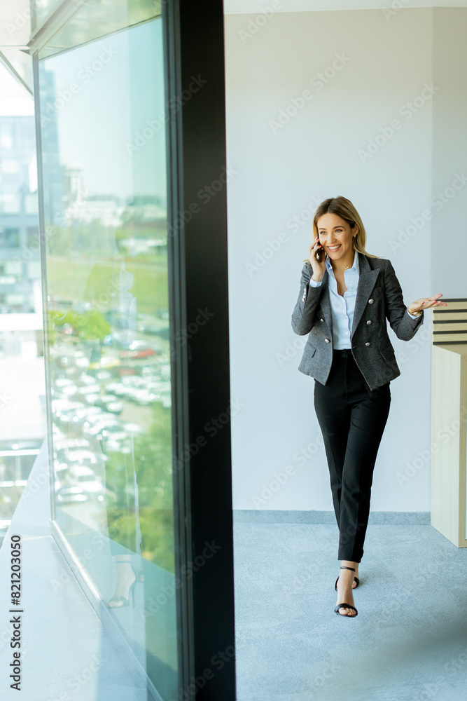 Young professional woman talking on mobile phone by office window on a sunny day Young professional woman talking on mobile phone by office window on a sunny day