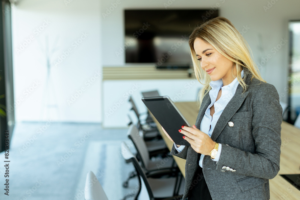 Smiling professional woman in red blazer holding tablet in modern conference room during daytime Smiling professional woman in red blazer holding tablet in modern conference room during daytime