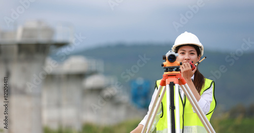 Portrait beautiful Asian construction engineer with a green safety vest hard hat and level survey camera.Engineer peering through a theodolite