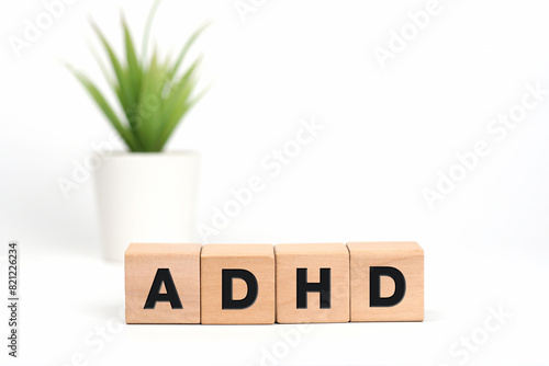 4 wooden cubes with letters on table with a pot of green plant on white background. The words written is ADHD Attention Deficit Hyperactivity Disorder acronym. Medical concept.Front View, Copy space.