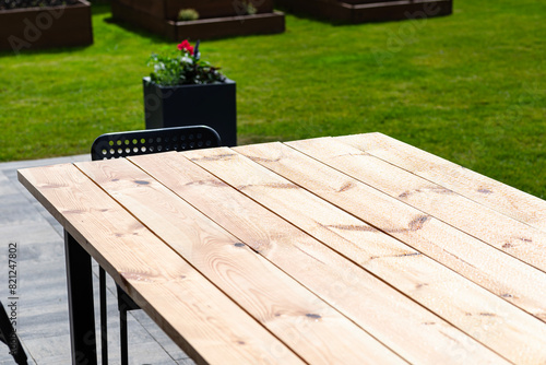 A modern table made of raw wood covered with yacht varnish, standing on the garden terrace.