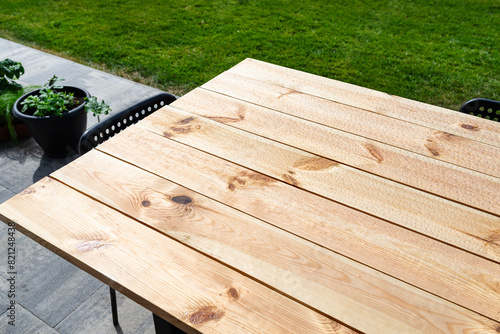 A modern table made of raw wood covered with yacht varnish, standing on the garden terrace.