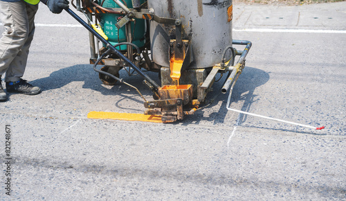 Man use thermoplastic road marking paint machine, hot melt marking paint machinery spraying a yellow line on concrete road.
