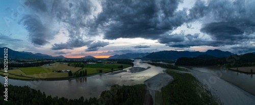 Fraser river by farm fields with mountains in background. Dramatic Sunset.
