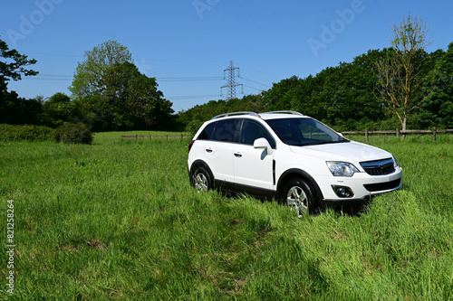 White SUV parked in a long grass field in the English countryside in summer time. 