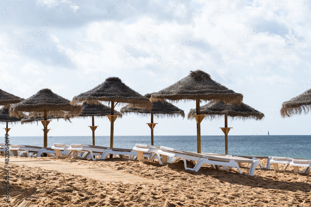 Straw chairs and umbrella. Praia do Peneco beach, Albufeira, Algarve, Portugal. Praia dos Pescadores beach. Fishermen, sunny day Straw chairs and umbrella. Praia do Peneco beach, Albufeira, Algarve, Portugal. Praia dos Pescadores beach. Fishermen, sunny day