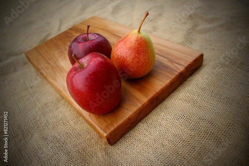 Fruits on a wooden cutting board - two red apples and a pear