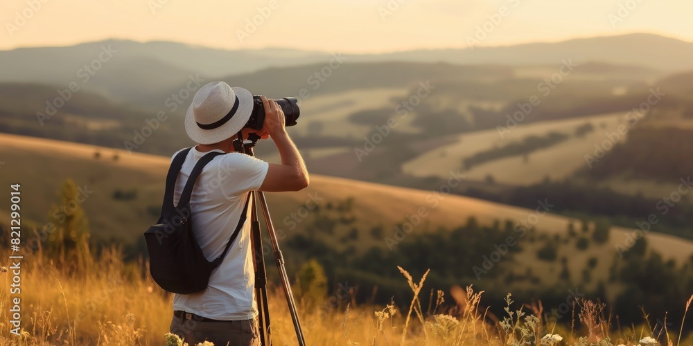 A photographer with a hat using a tripod and camera to take landscape photos at sunset