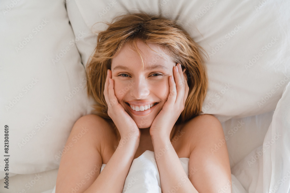 Smiling relaxed young woman waking up with good mood starting new day on orthopedic mattress with white linen bedsheets on weekends Smiling relaxed young woman waking up with good mood starting new day on orthopedic mattress with white linen bedsheets on weekends