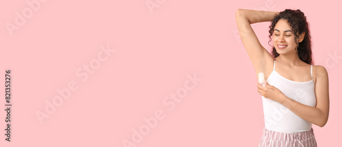 Beautiful young African-American woman applying deodorant on pink background with space for text © Pixel-Shot