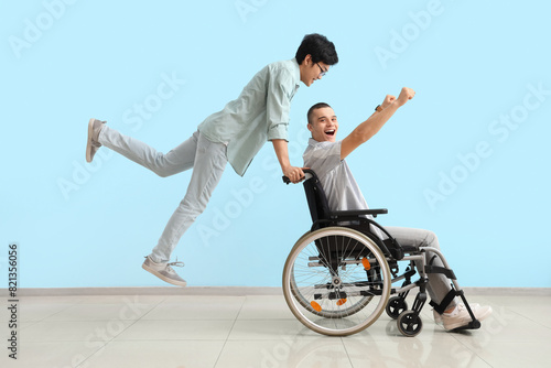 Jumping teenage boy with his friend in wheelchair near blue wall