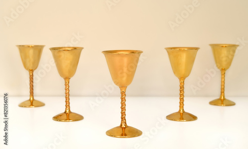 Five golden antique goblets with high stems on the white table. Close-up. Selective focus. Copy space. 