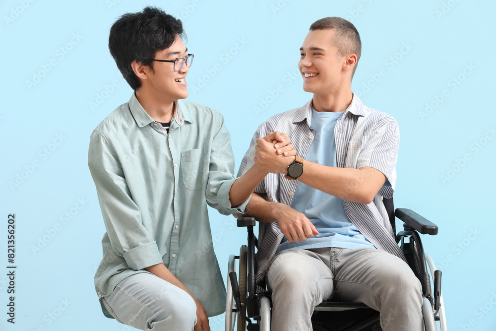 Teenage boy with his friend in wheelchair holding hands on blue background Teenage boy with his friend in wheelchair holding hands on blue background