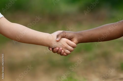 A close up of two hands of children. two little kids shaking hands against a green nature background. © MeSSrro