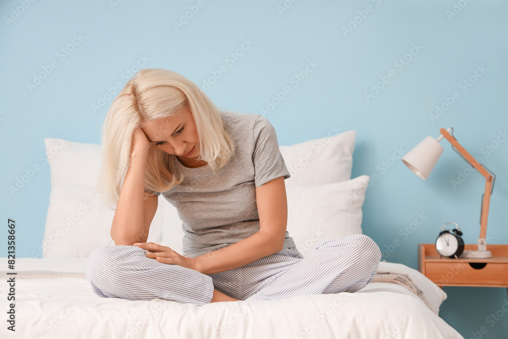 Depressed mature woman sitting on bed in bedroom