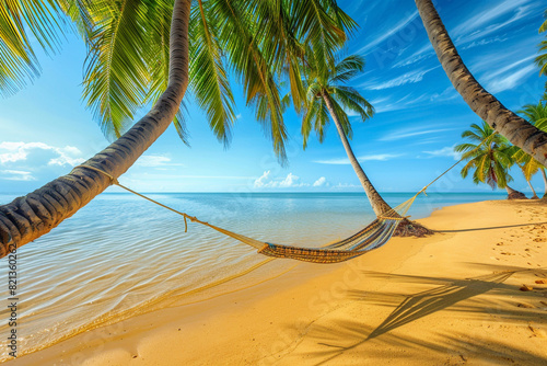 A tropical beach scene with smooth golden sand and shallow, calm water, with a hammock tied between two palm trees under a bright blue sky © Ateeq