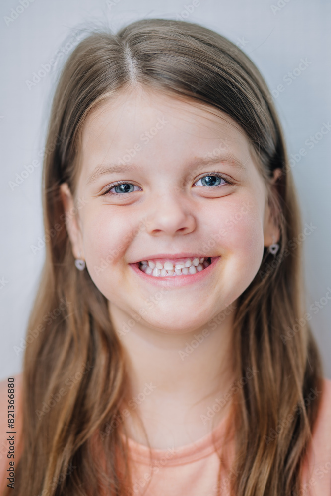 A smiling young girl with long brown hair and blue eyes, wearing a peach-colored shirt and small heart-shaped earrings... A smiling young girl with long brown hair and blue eyes, wearing a peach-colored shirt and small heart-shaped earrings...