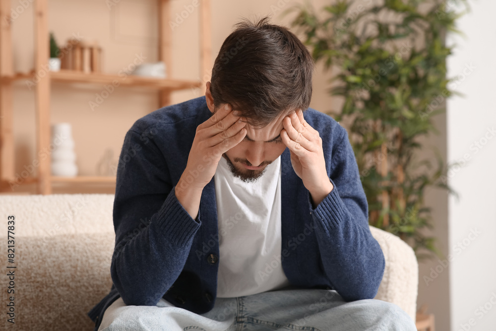 Tired young man with headache sitting on sofa at home Tired young man with headache sitting on sofa at home