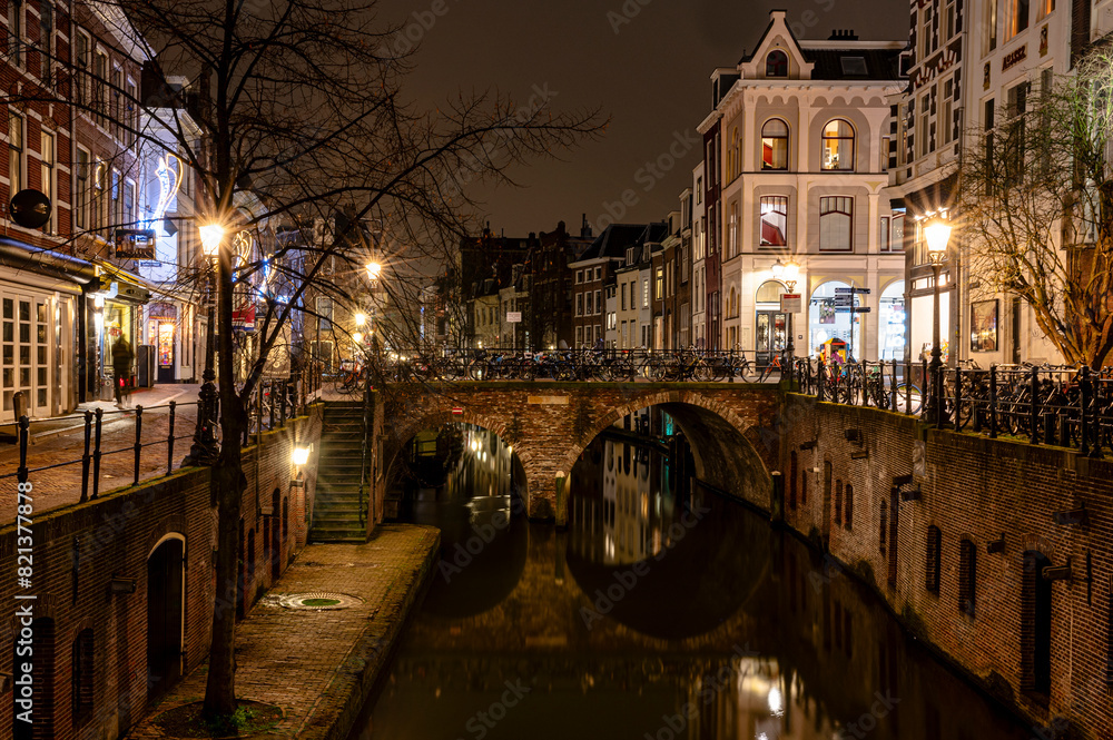 Naklejka premium A street in the city Utrecht at night with a bridge over a canal. The street is lit up with lights and the buildings are old