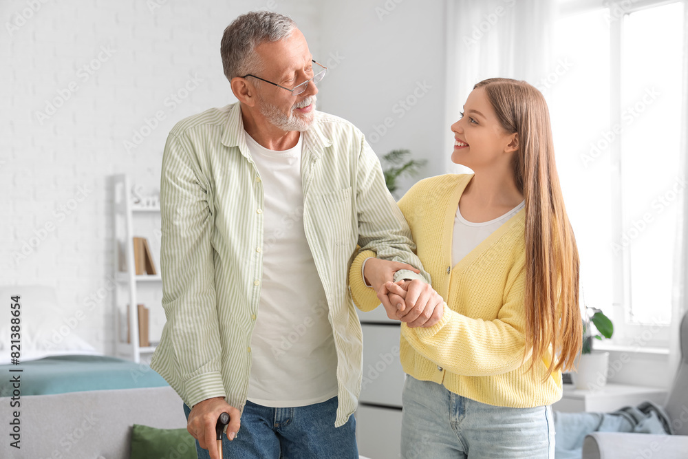 Female caregiver helping senior man with walking stick in nursing home Female caregiver helping senior man with walking stick in nursing home