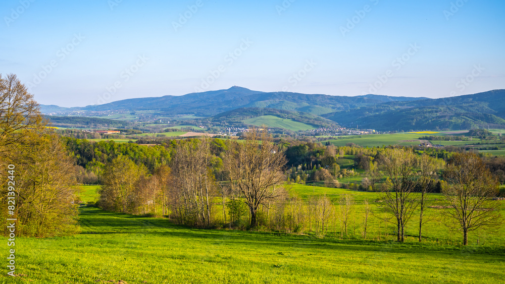 A breathtaking view of the Jested Ridge horizon, captured from a lush green field under a clear blue sky. The serene atmosphere suggests early morning or late afternoon. Located in Czech Republic