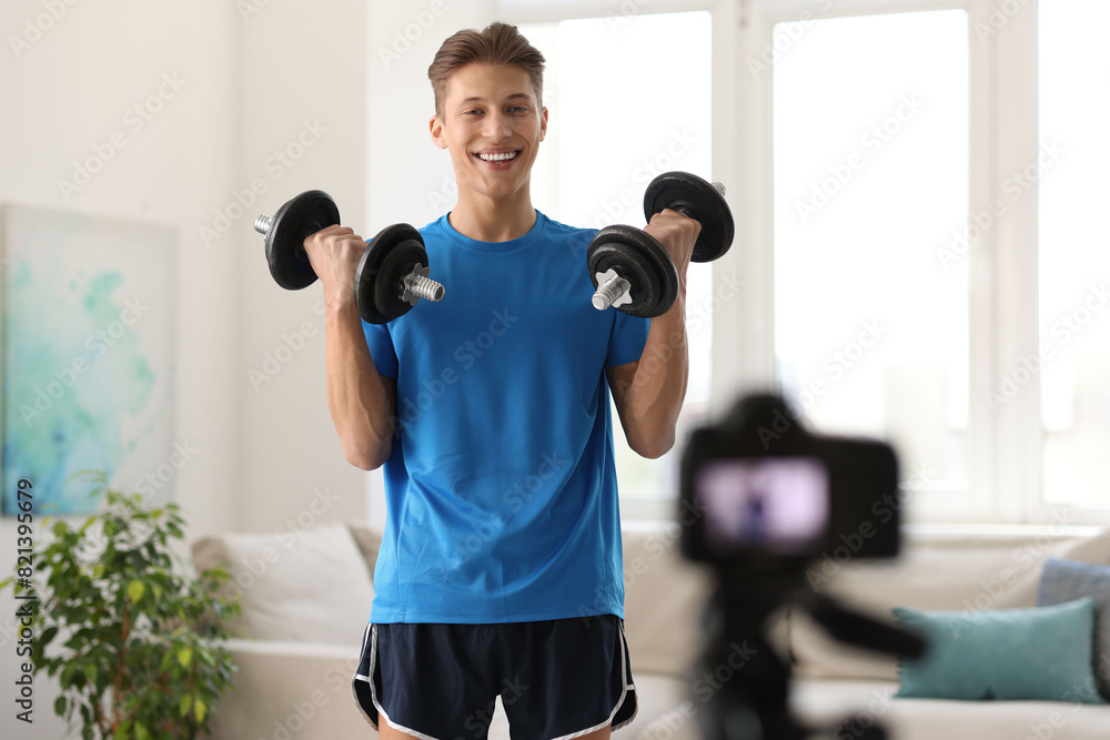 Smiling sports blogger working out with dumbbells while recording fitness lesson at home Smiling sports blogger working out with dumbbells while recording fitness lesson at home