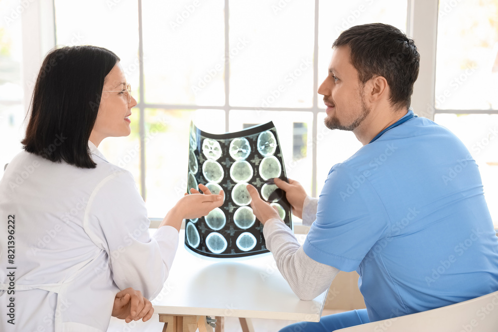 Doctors studying MRI scan at table in clinic, back view Doctors studying MRI scan at table in clinic, back view
