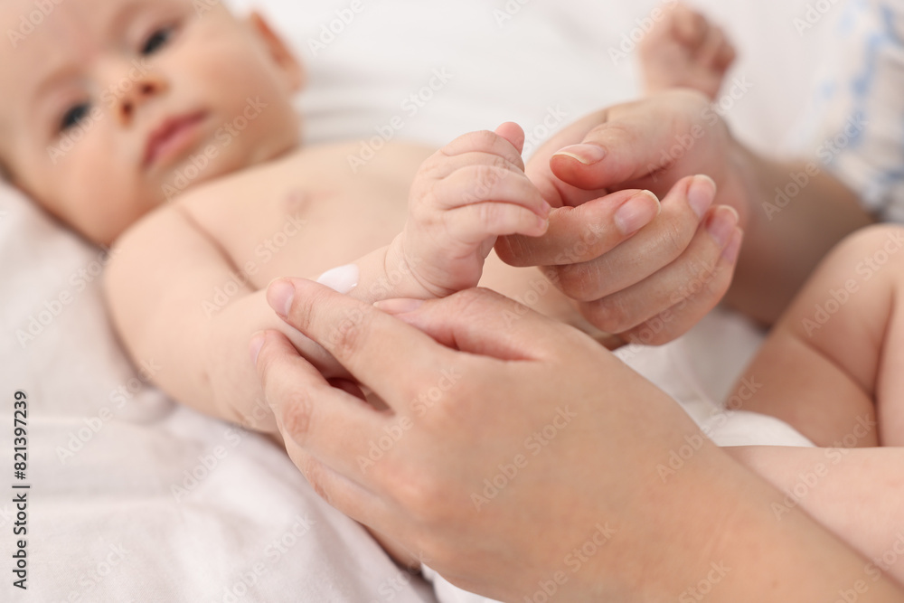 Woman applying body cream onto baby`s skin on bed, closeup Woman applying body cream onto baby`s skin on bed, closeup