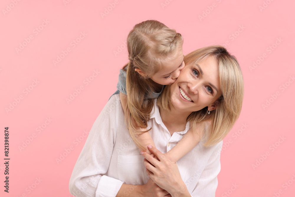 Daughter hugging and kissing her happy mother on pink background Daughter hugging and kissing her happy mother on pink background