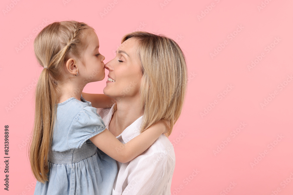 Daughter hugging and kissing her happy mother on pink background. Space for text Daughter hugging and kissing her happy mother on pink background. Space for text