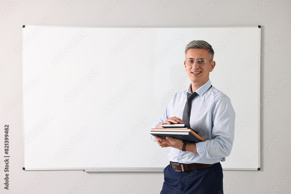 Teacher with notebooks near whiteboard in classroom Teacher with notebooks near whiteboard in classroom