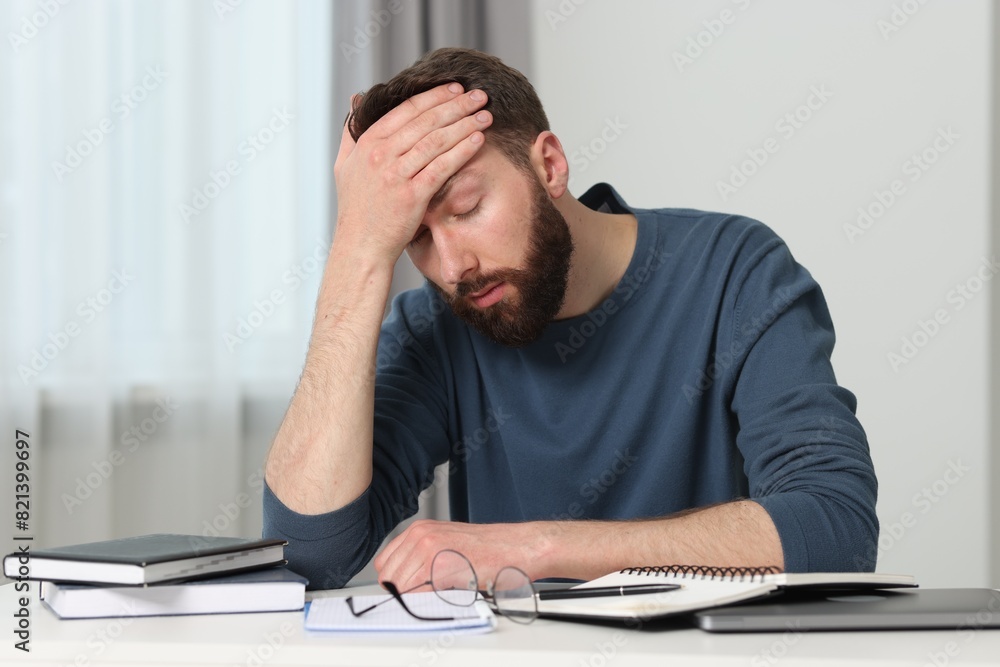 Overwhelmed man suffering from headache at table indoors Overwhelmed man suffering from headache at table indoors