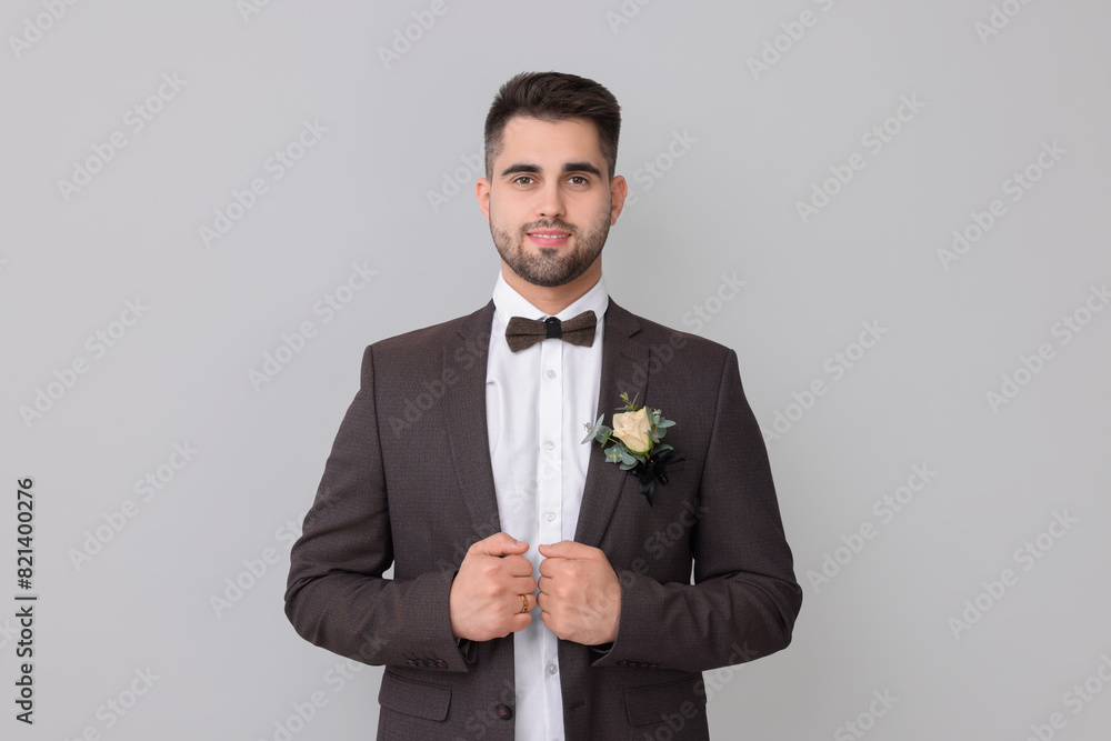 Handsome young groom with boutonniere on light grey background. Wedding accessory